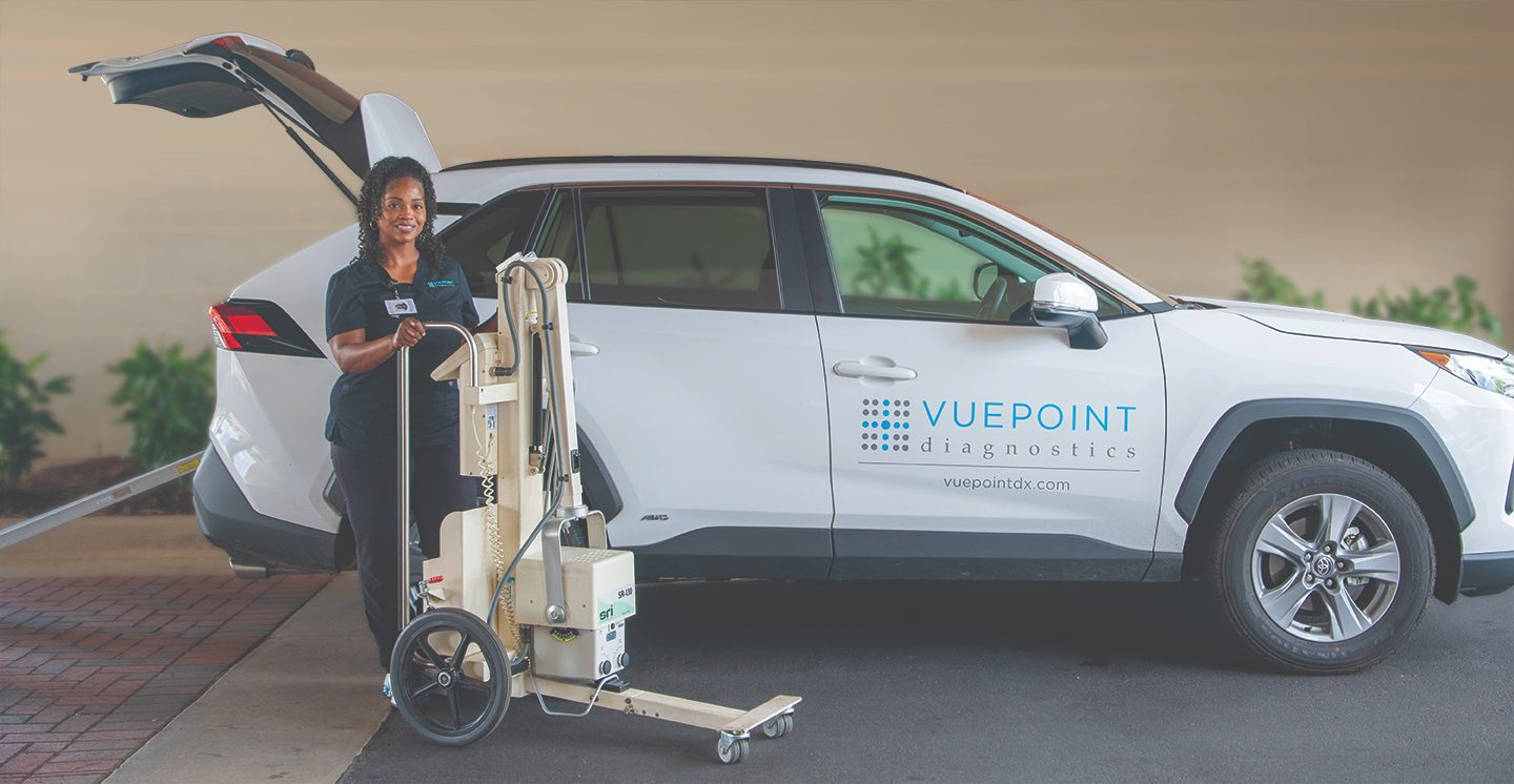 A VuePoint technologist standing beside a branded SUV with a portable X-ray unit, ready for an in-home visit